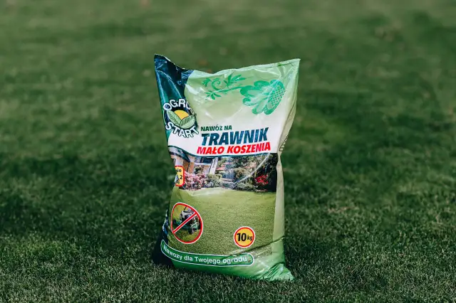 Zielona torba z nawozem do trawnika na tle trawy.