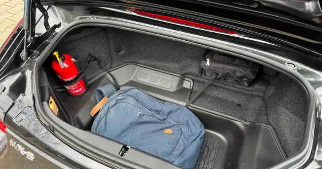 Czerwona gaśnica i niebieski plecak w bagażniku samochodu.