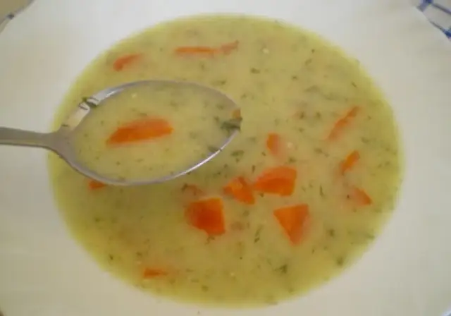 Łyżka zupy śmietanowej z marchewką i koperkiem na białym talerzu.