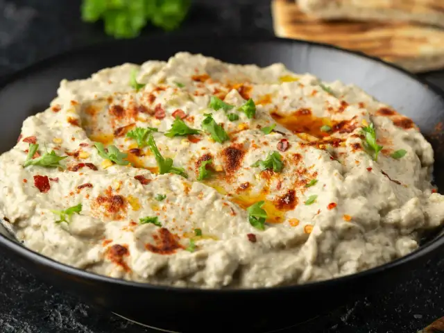 Kremowa pasta z bakłażana, doprawiona papryką i posypana natką pietruszki, w czarnej misce. Idealna do pieczywa.
