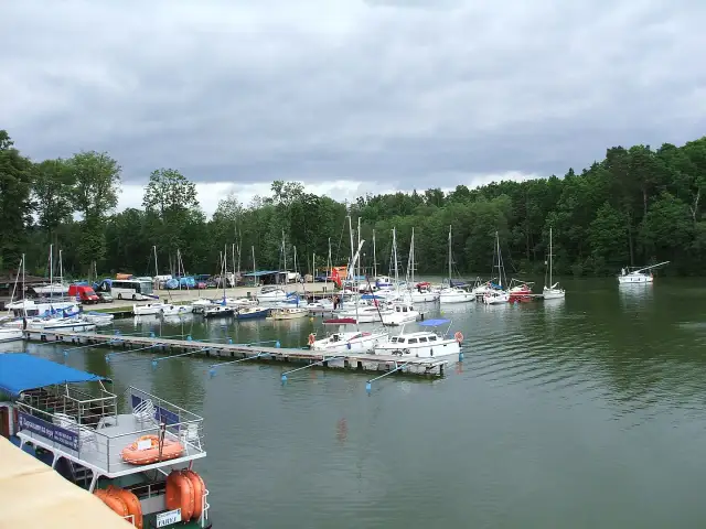 Port w Rucianem Nidzie pełen żaglówek i łodzi. W tle las i pochmurne niebo.