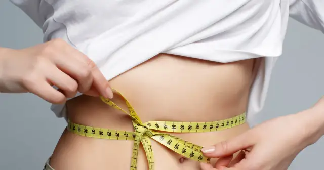 Kobieta mierzy talię centymetrem, szukając odpowiedzi na pytanie, jak szybko schudnąć.
