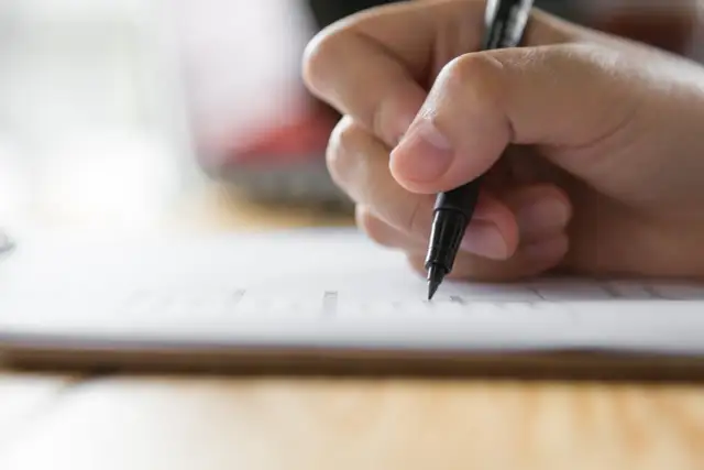 Dłoń pisze piórem po papierze. Czy można skończyć technikum bez egzaminu zawodowego? Zastanawiam się nad tym, wypełniając dokumenty.