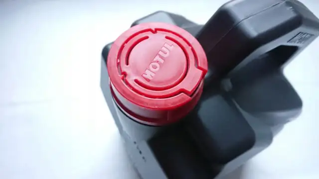 Czarne opakowanie oleju Motul z czerwoną zakrętką z logo.