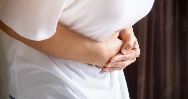 Osoba trzyma się za brzuch, odczuwając ostry ból w lewym boku.