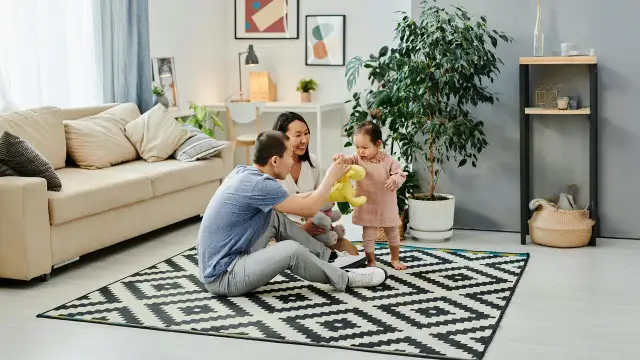 Rodzice bawią się z dzieckiem na dywanie w salonie.