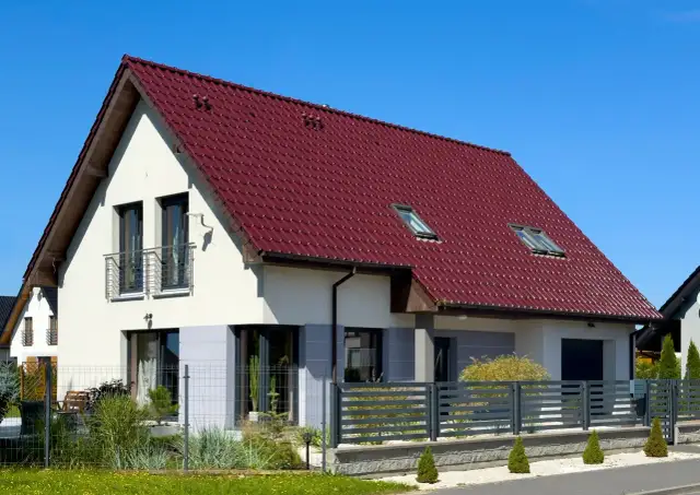 Nowoczesny dom z czerwonym dachem i ogrodzeniem.