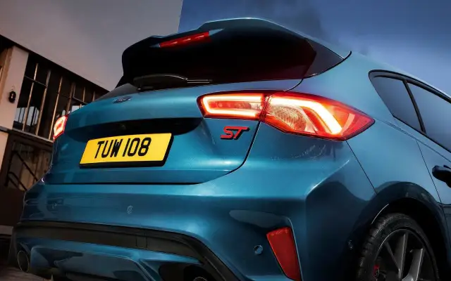 Tylna część sportowego Forda Focus ST 2025 w kolorze niebieskim, z podświetlonymi światłami i czerwonym emblematem ST.