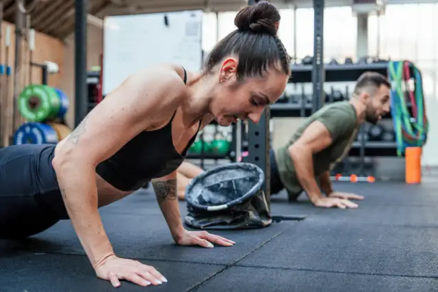 Kobieta i mężczyzna wykonują pompki na siłowni CrossFit.
