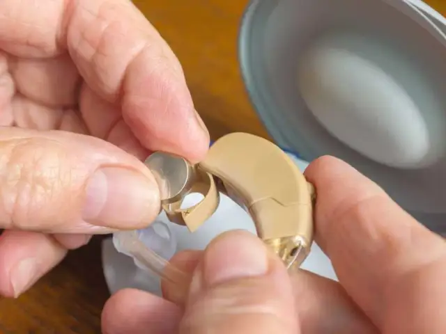 Dłoń wkłada baterię do aparatu słuchowego.