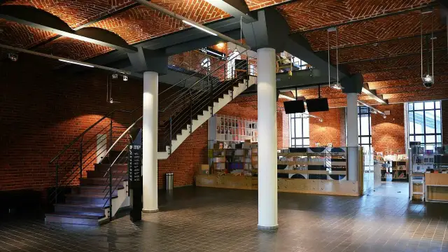 Wnętrze muzeum sztuki współczesnej z ceglanymi ścianami, łukowym sufitem i schodami.