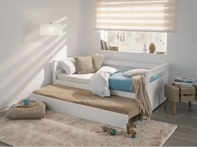 Cama nido blanca con colchones, cojines y manta en un dormitorio juvenil.