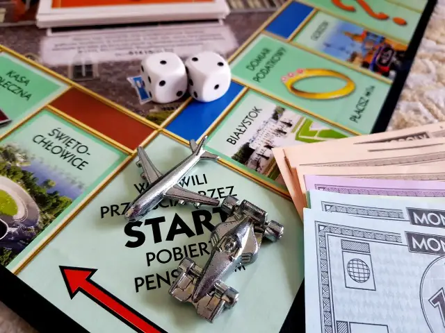 Plansza Monopoly z pionkami (samolot, bolid), kostkami i banknotami.