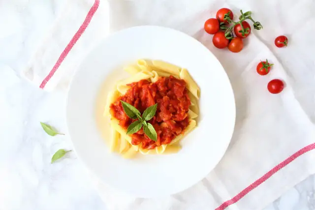 Penne z sosem pomidorowym i bazylią, obok świeże pomidorki koktajlowe.