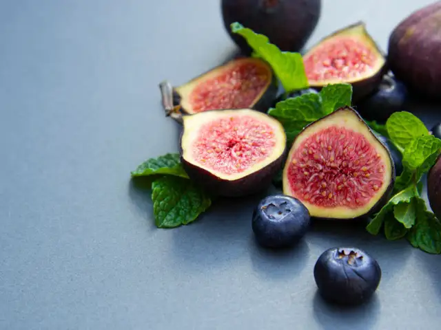 Słodki, soczysty figa owoc, przekrojony na pół, z jagodami i listkami mięty na szarym tle.