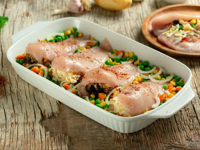 Surowe piersi kurczaka nadziewane ryżem i warzywami w naczyniu żaroodpornym.