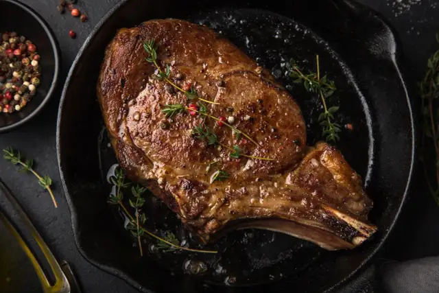 Soczysty stek wołowy z ziołami i pieprzem na patelni.