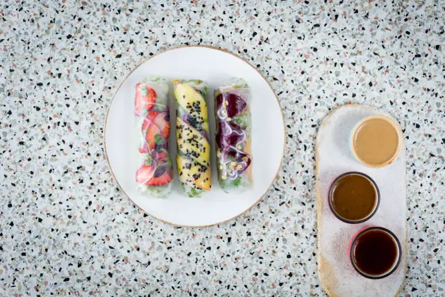 Trzy rolki papieru ryżowego z warzywami i owocami: truskawki, mango z czarnym sezamem, buraki. Obok sosy.