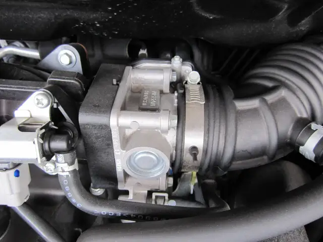 Widok na przepustnicę silnika Nissana, gdzie jest zamontowana w układzie dolotowym, otoczona przewodami i elementami silnika.