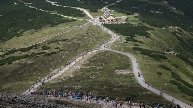 Tłum turystów podąża szlakiem na Śnieżkę, wspinając się po kamienistym zboczu.