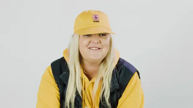 Frau mit gelber Kappe und Kapuzenpullover lächelt.