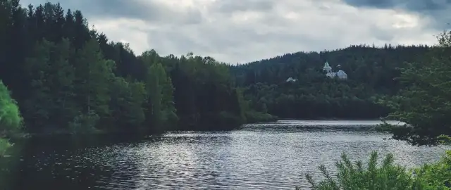 Spokojne jezioro Czerniańskie otoczone gęstym lasem, z widocznym na wzgórzu pałacem.
