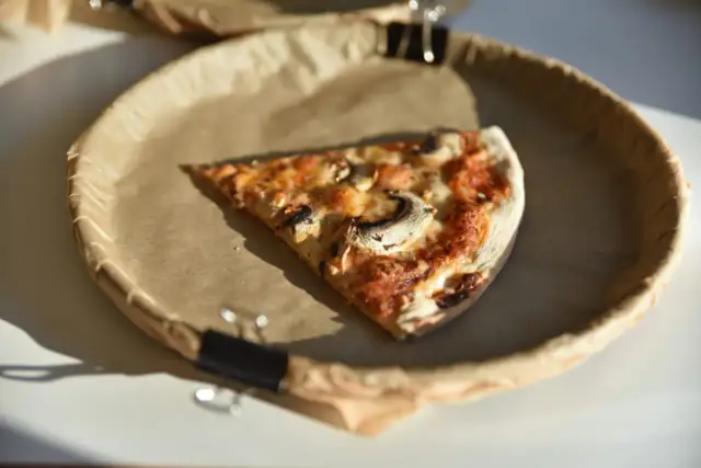 Jeden kawałek pizzy z pieczarkami na brązowym papierze. Ciekawe, ile kawałków ma cała pizza?