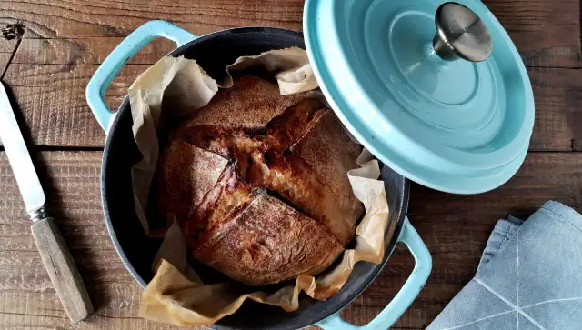 Świeżo upieczony chleb na zakwasie w niebieskim naczyniu żeliwnym, gotowy do krojenia.