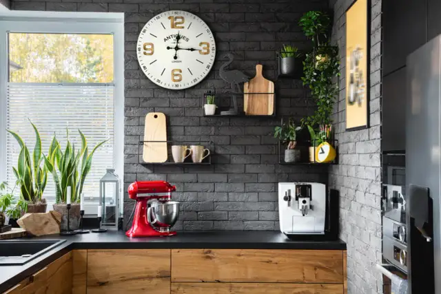 Nowoczesna kuchnia z czarną cegłą, zegarem, roślinami i czerwonym mikserem.