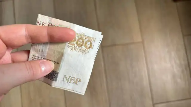 Dłoń trzyma banknot 200 zł. Gdzie można trzymać pieniądze? Familiada podpowie!