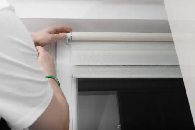 Dłoń naprawia mechanizm rolety dzień-noc.