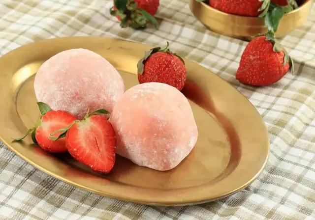 Różowe mochi z truskawkami na złotym talerzu.