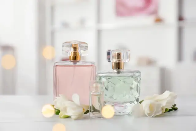 Szukasz inspiracji, jakie perfumy z Rossmanna polecacie? Na zdjęciu eleganckie flakoniki z różowymi i zielonymi perfumami, ozdobione białymi kwiatami.