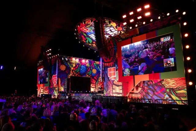 Kolorowa scena festiwalu Poland Rock 2026 z wielkim ekranem pokazującym publiczność. Tłum widzów wpatrzony w widowisko.