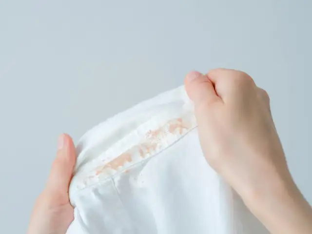 Dłonie trzymają białą bluzkę z plamami podkładu na kołnierzyku.