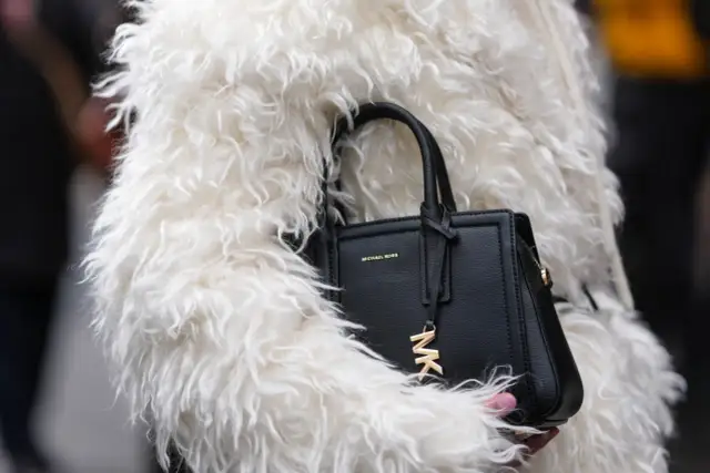 Czarna torebka Michael Kors z logo MK, otulona w białe futro. To marka znana z luksusowych akcesoriów.