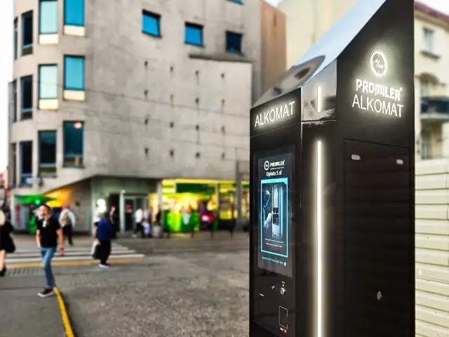 Alkomat Promiler na ulicy, z budynkami i ludźmi w tle.