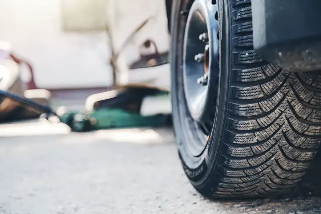 Zimowa opona z bieżnikiem skierowanym w dobrym kierunku, gotowa do montażu. W tle podnośnik samochodowy.