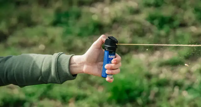 Dłoń trzymająca niebieski gaz pieprzowy, z którego wydobywa się strumień.