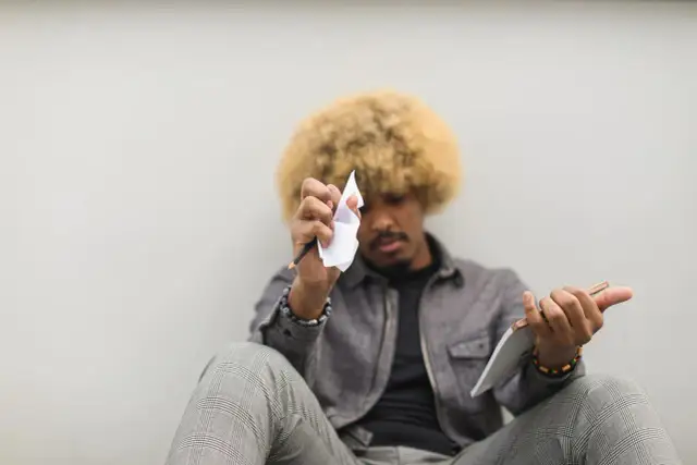 Mężczyzna z afro włosami siedzi, trzymając ołówek i zmiętą kartkę papieru.