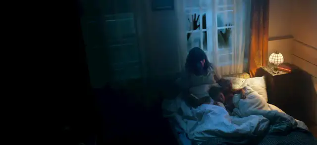 Dziecko śpi, gdy matka czyta mu bajkę. Za oknem widać przerażające dłonie, zapowiadające 28 dni grozy.