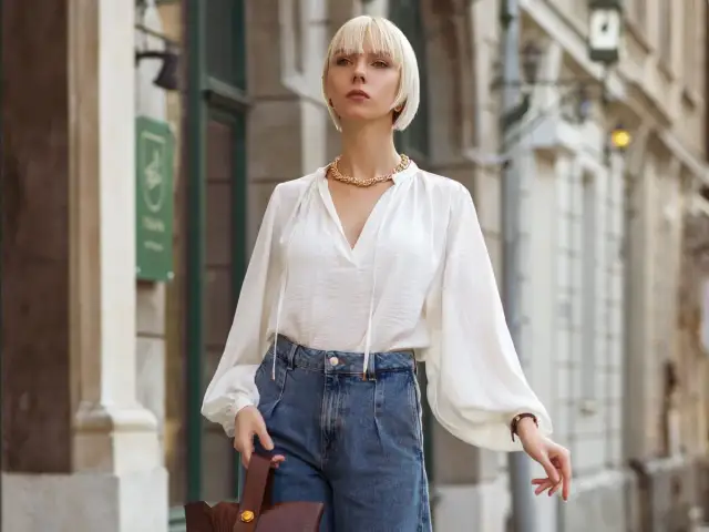 Elegancka biała bluzka z bufiastymi rękawami i jeansowe, szerokie spodnie. Idealna stylizacja, która odpowiada na pytanie: jaka bluzka do szerokich spodni.