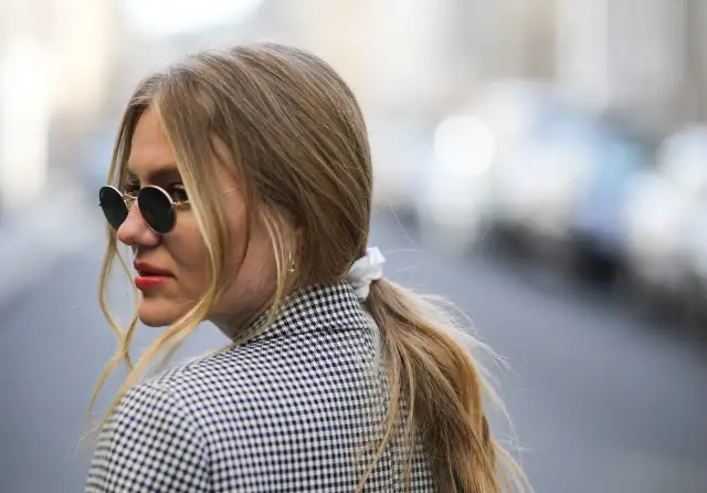 Kobieta w okularach przeciwsłonecznych i marynarce w kratkę, z blond kucykiem.