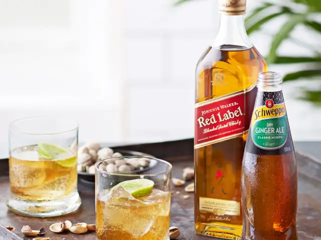 Butelka Johnnie Walker Red Label, butelka Schweppes Ginger Ale i dwa drinki z lodem i limonką.