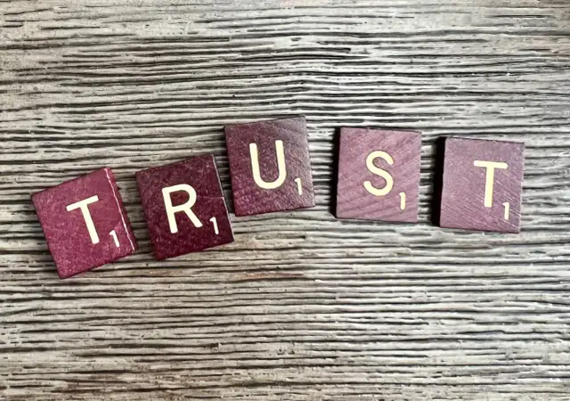 Litery "TRUST" ułożone na drewnianym tle. Brak zaufania w związku czy to ma sens?