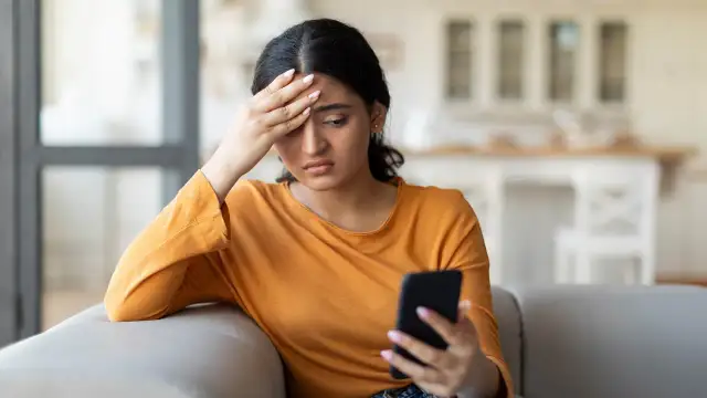 Zmartwiona kobieta z telefonem w dłoni zastanawia się, co napisać byłemu żeby odpisał.