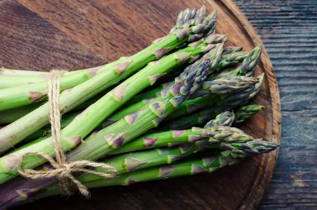 Pęczek zielonych szparagów związany sznurkiem na drewnianej desce.