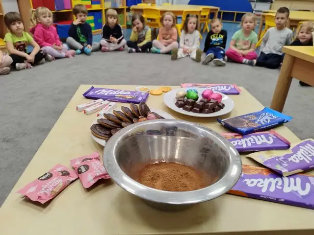 Dzieci czekają na słodkie pomysły na dzień czekolady. Na stole czekają czekolady Milka, Kinder i ciastka.