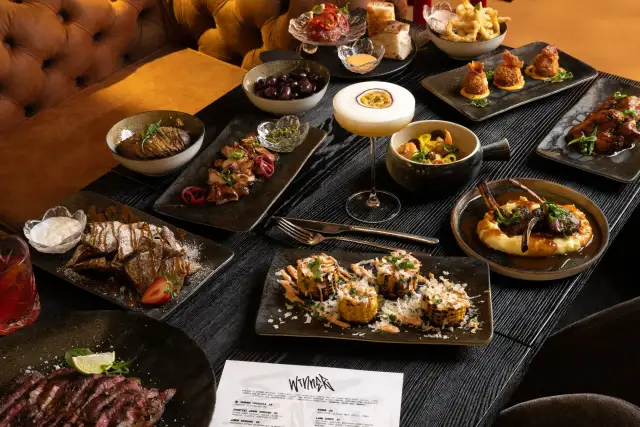 Stół z różnorodnymi daniami: mięsa, ryby, warzywa, deser i drinki.