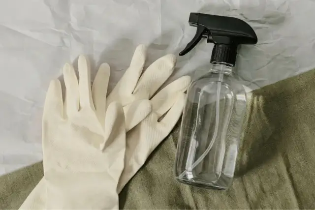 Para gumowych rękawiczek i butelka z atomizerem na zielonym tle.